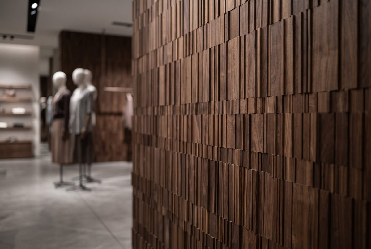 A close-up of a dark brown wooden slat wall with a blurred boutique interior and mannequins in the background.
